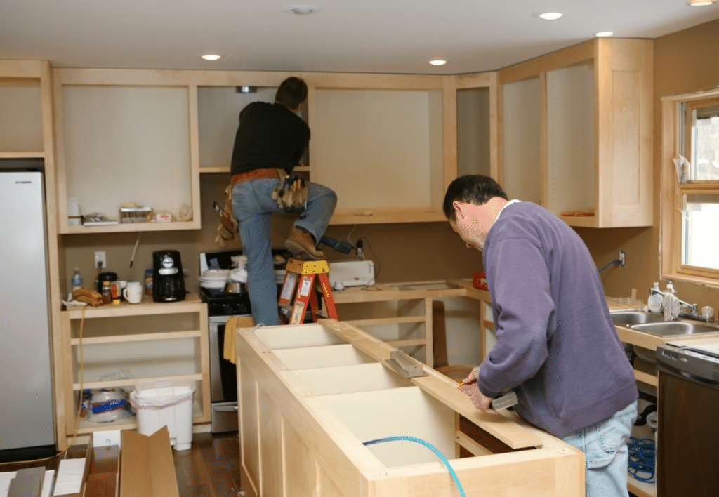 a cabinetmaker installing custom-made kitchen island while electrician installs cabinet lighting