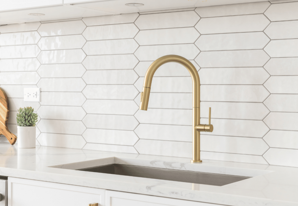 Kitchen design with tiled backsplash, white shaker cabinets and gold faucet
